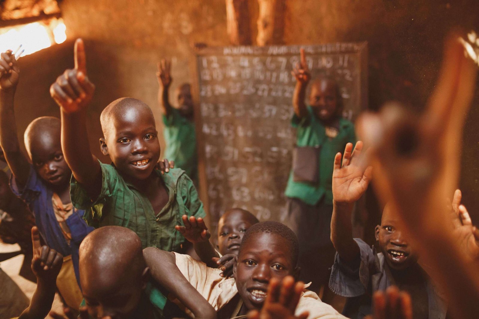 Pupils in a rural classroom raising their hands and giving thumbs up
